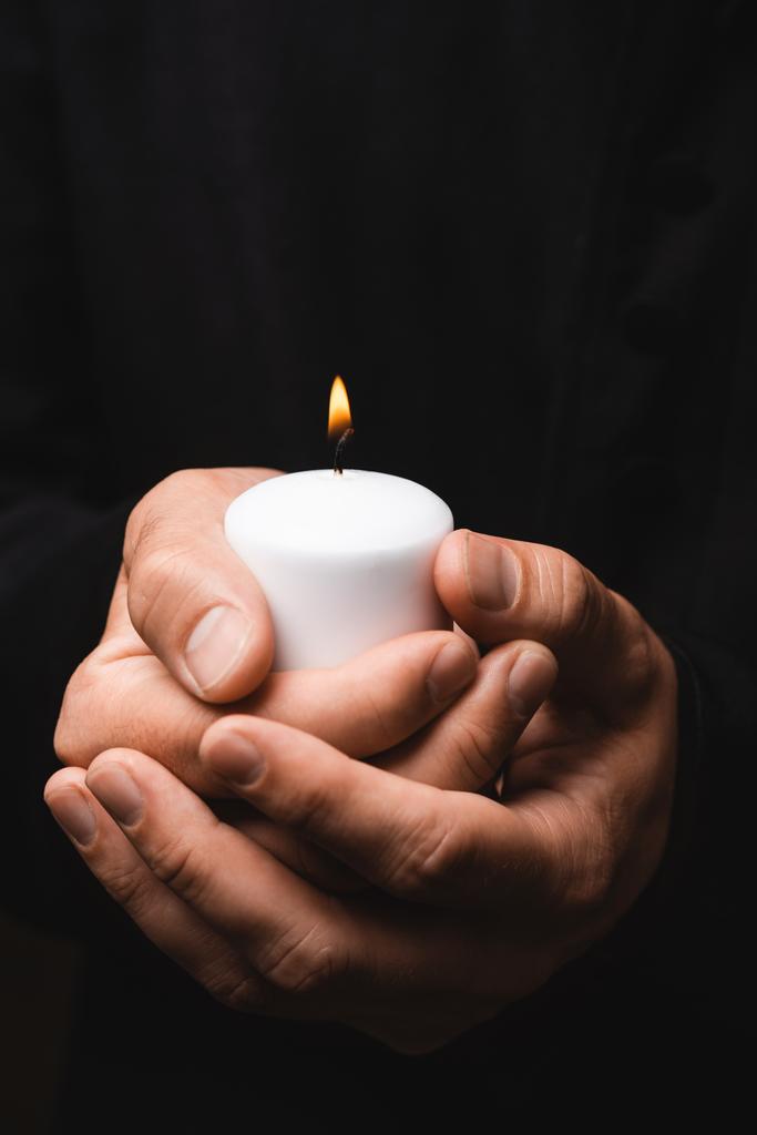 oříznutý pohled na kněze držícího hořící svíčku izolovanou na černém  - Fotografie, Obrázek