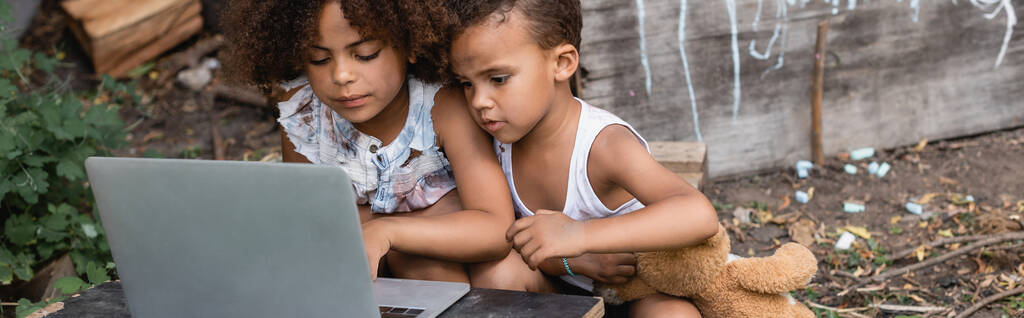 panoramische oriëntatie van arme Afrikaans-Amerikaanse kinderen met behulp van laptop buiten  - Foto, afbeelding