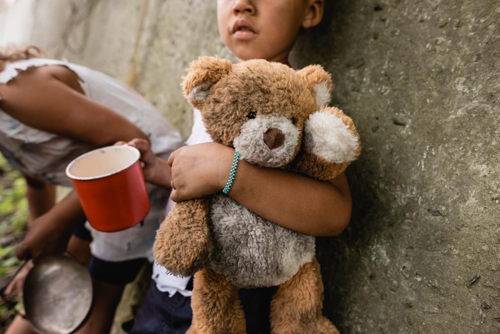 Vista recortada de niños afroamericanos sin hogar con oso de peluche sucio mendigando limosnas en el tugurio
  - Foto, imagen