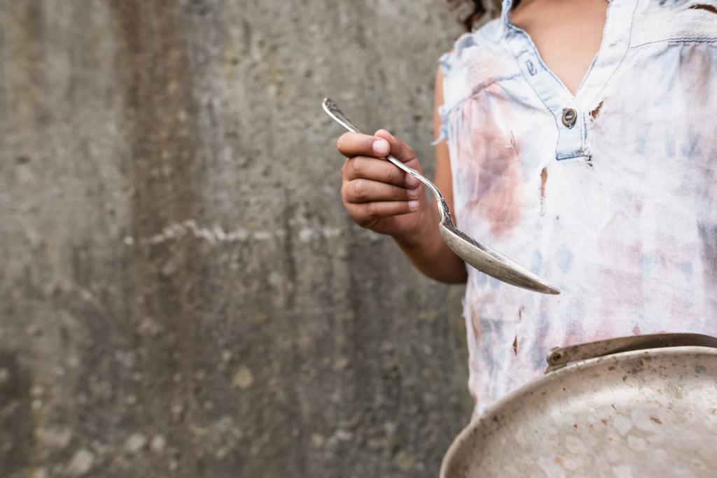 Vista cortada da criança afro-americana segurando placa de metal e colher suja na rua urbana
  - Foto, Imagem