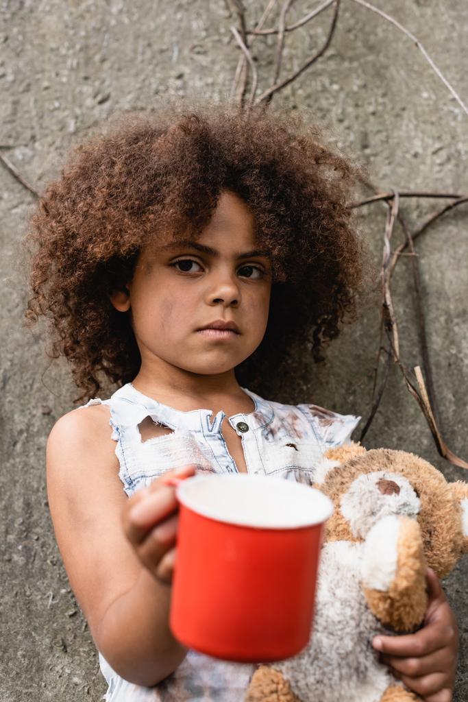 Selektiver Fokus mittelloser afrikanisch-amerikanischer Kinder mit schmutzigem Teddybär, der Almosen auf urbanen Straßen erbettelt  - Foto, Bild