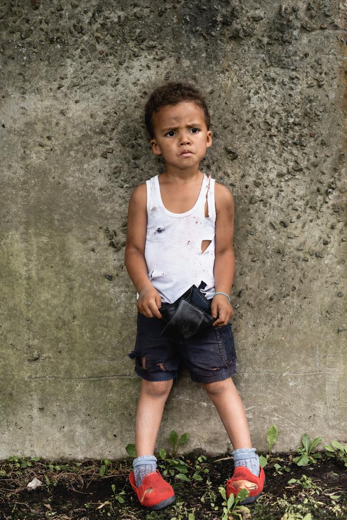 Zaniepokojony afrykański chłopiec w brudnych ciuchach z pustym portfelem na miejskiej ulicy  - Zdjęcie, obraz