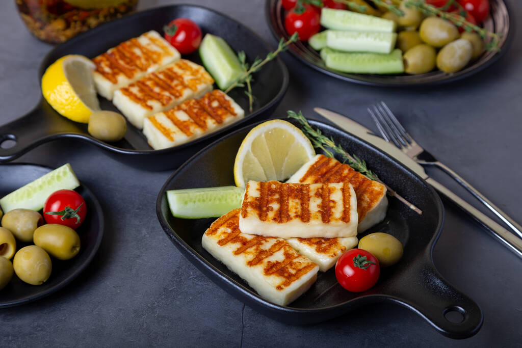 Grilled haloumi cheese on a black pan with olives, tomatoes, cucumbers and pepperoni. Close-up. - Photo, Image