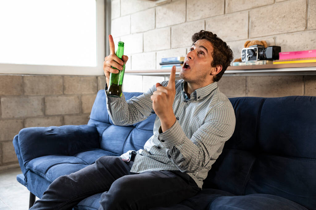 knappe en elegante man die thuis tv kijkt en bier drinkt in de woonkamer - Foto, afbeelding