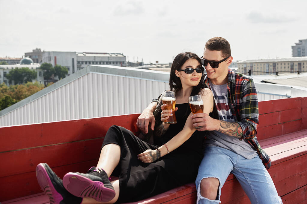 Joyeux couple souriant trinquant et buvant de la bière au pub extérieur ou au bar sur le toit en été, espace de copie - Photo, image
