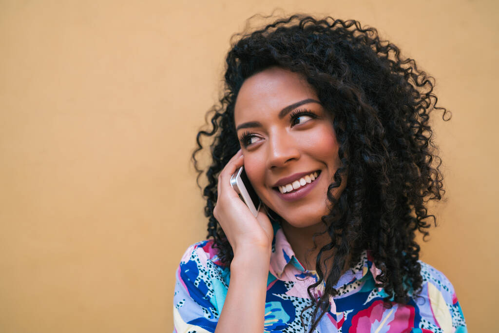 Egy fiatal afro nő portréja, aki sárga háttérrel beszél telefonon. Kommunikációs elv. - Fotó, kép