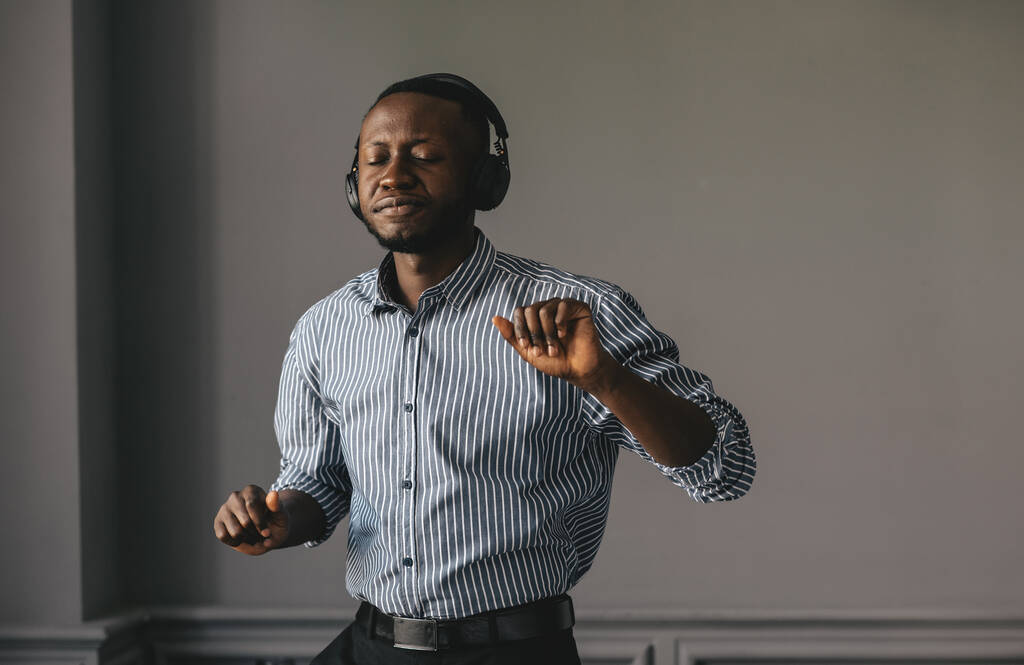 чорний молодий чоловік в навушниках танцює на музиці на сірому фоні
 - Фото, зображення