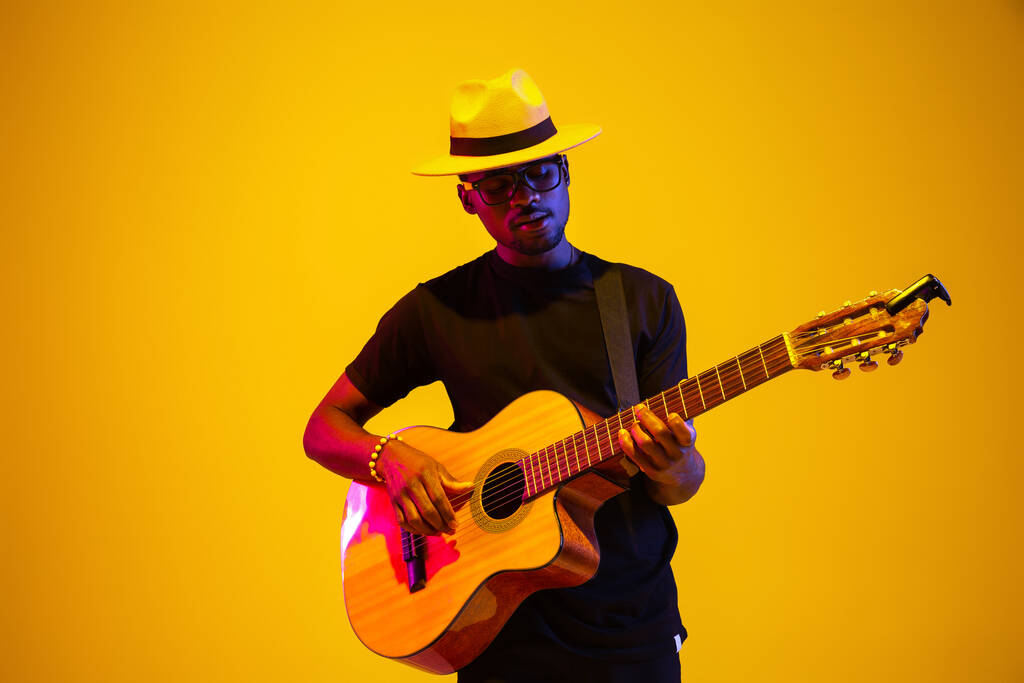 Fiatal afro-amerikai zenész énekel, gitározik neon fényben - Fotó, kép