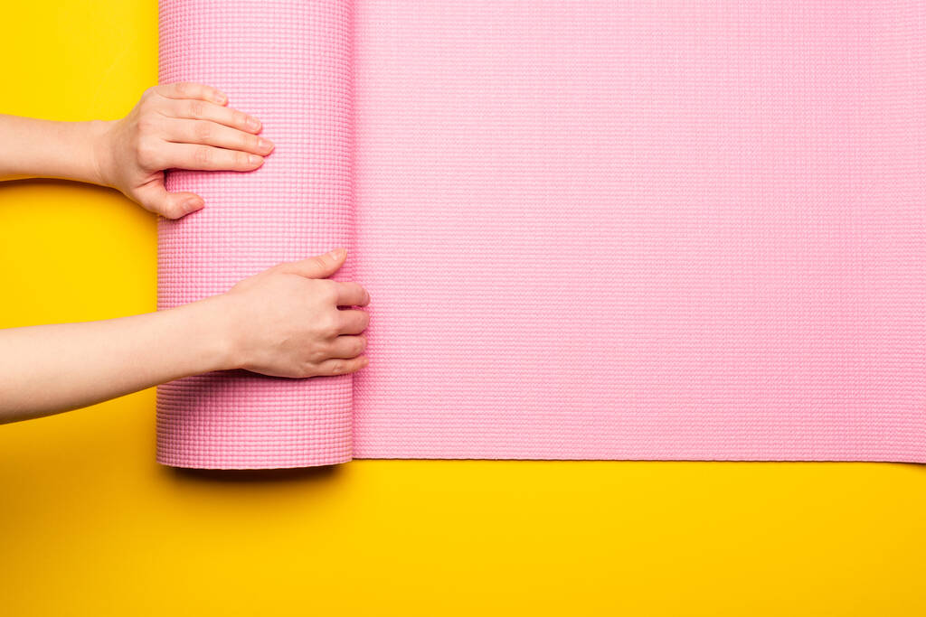 vue recadrée de femme déroulant tapis de fitness rose sur fond jaune - Photo, image