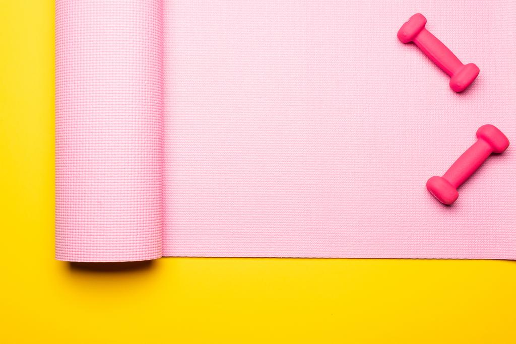 felső nézet rózsaszín fitness szőnyeg és súlyzók sárga háttér - Fotó, kép