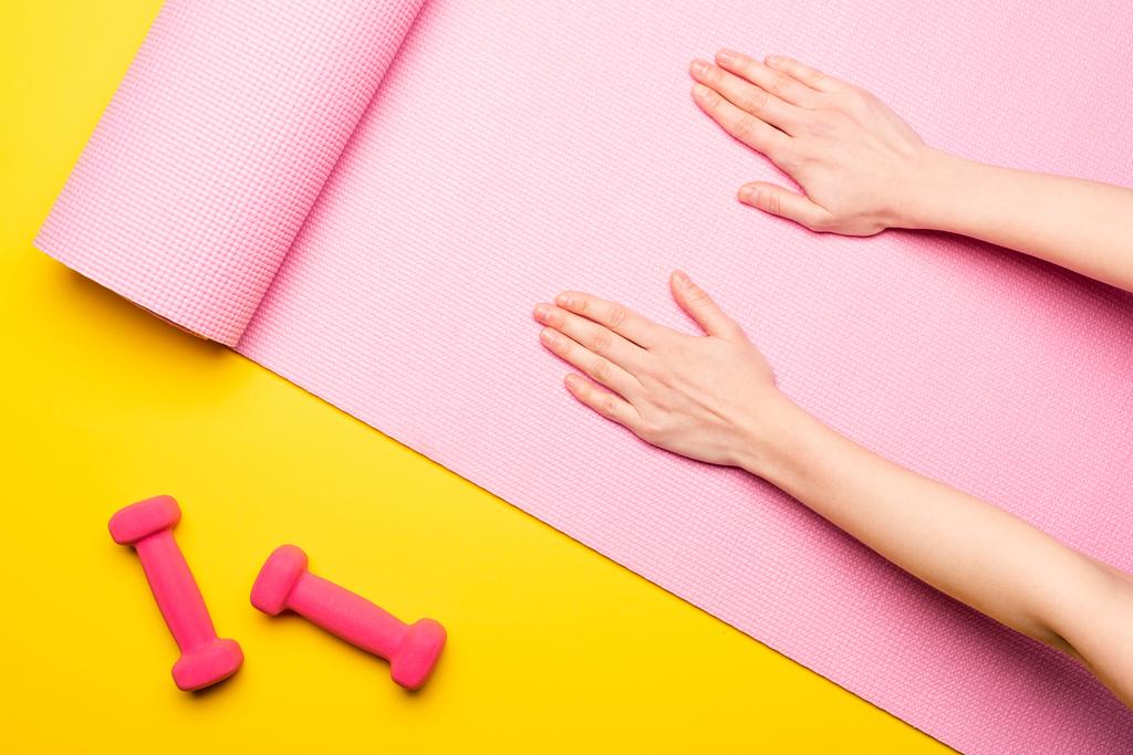 ピンクのフィットネスマットの女性の手のトップビュー黄色の背景にダンベルの近く - 写真・画像