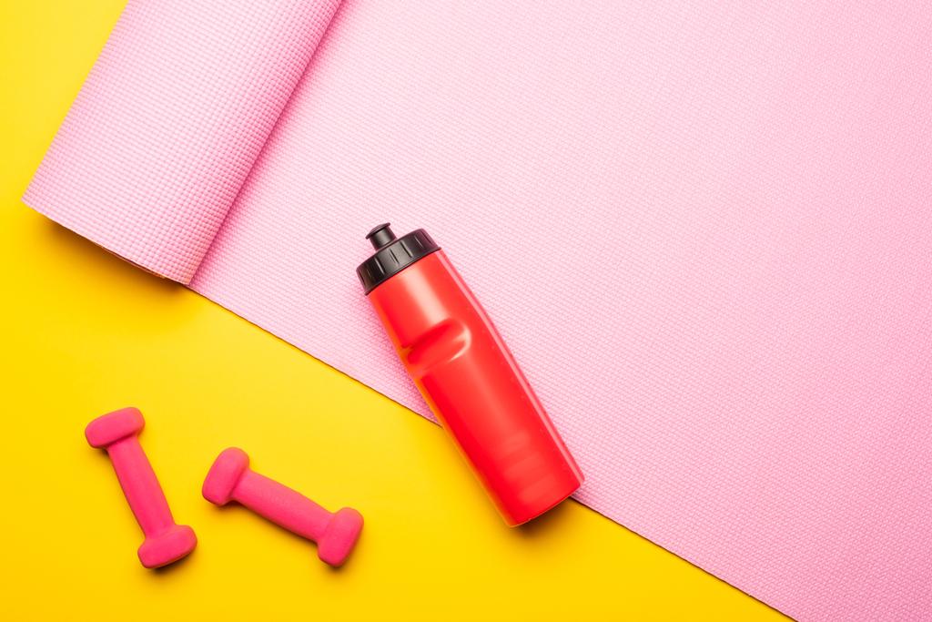 вид зверху на червону спортивну пляшку, рожевий фітнес-матер і гантелі на жовтому фоні
 - Фото, зображення