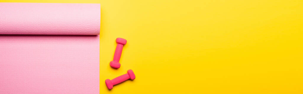 Sarı arkaplanda pembe fitness paspasının ve dambılların üst görüntüsü, panoramik çekim - Fotoğraf, Görsel