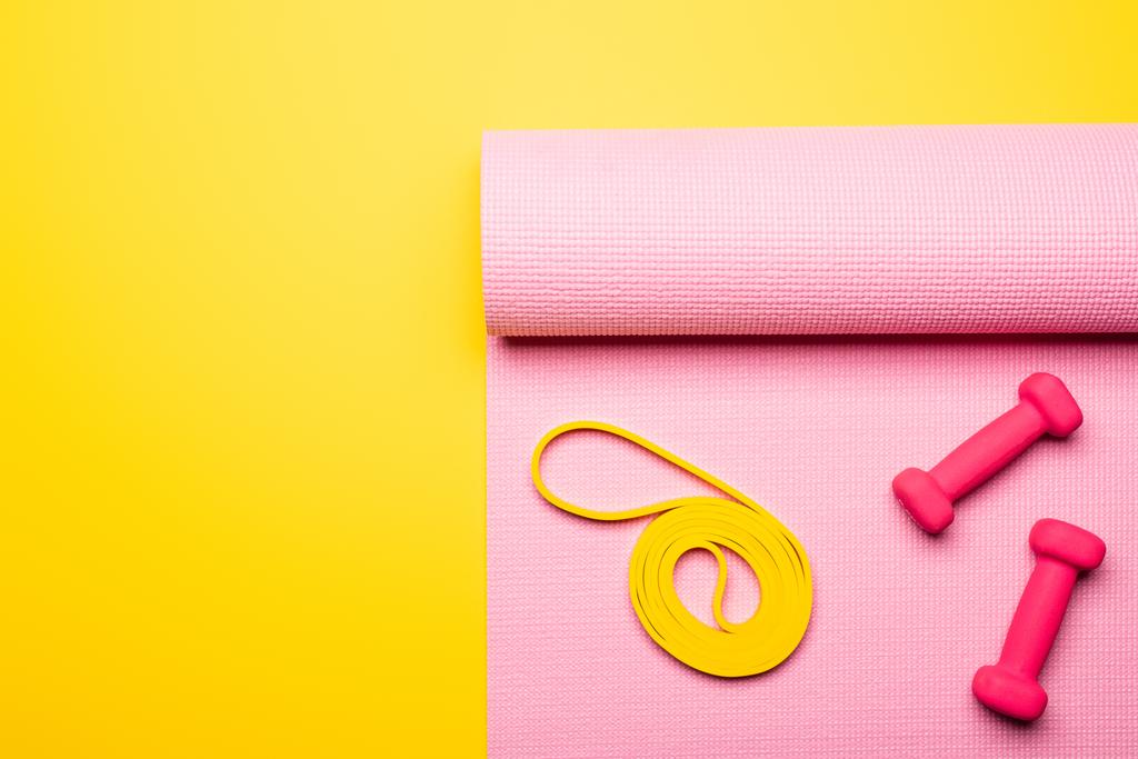 top view of pink dumbbells and elastic band on pink fitness mat on yellow background - Photo, Image