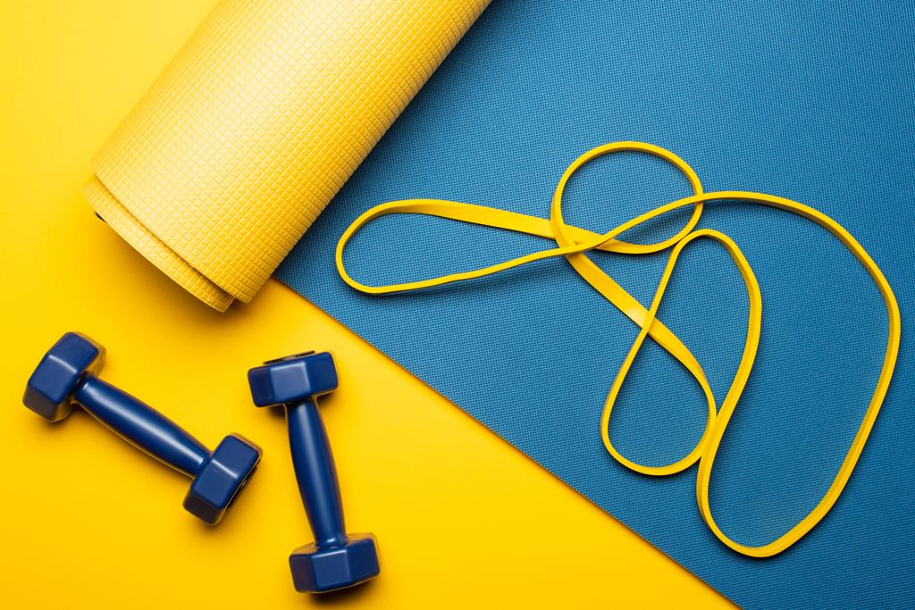 vista superior de la esterilla de fitness azul con mancuernas y banda de resistencia sobre fondo amarillo
 - Foto, imagen