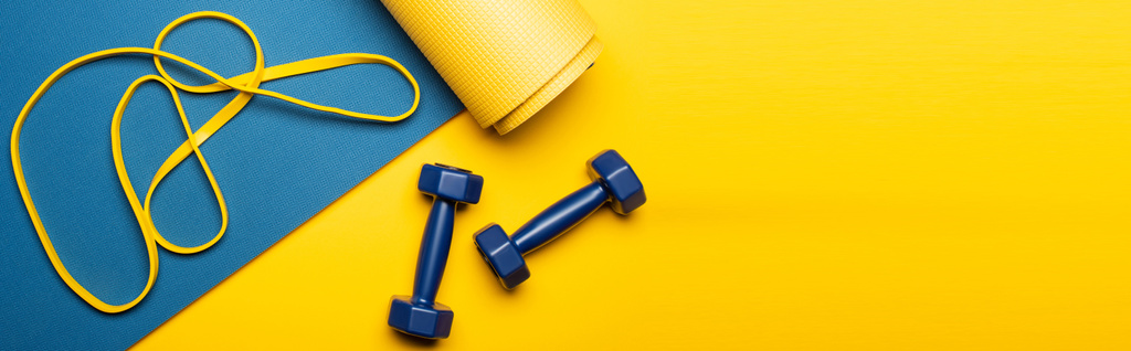 vista superior do tapete de fitness azul com halteres e banda de resistência no fundo amarelo, tiro panorâmico
 - Foto, Imagem