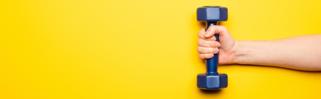 cropped view of woman holding blue dumbbell on yellow background, panoramic shot - Photo, Image