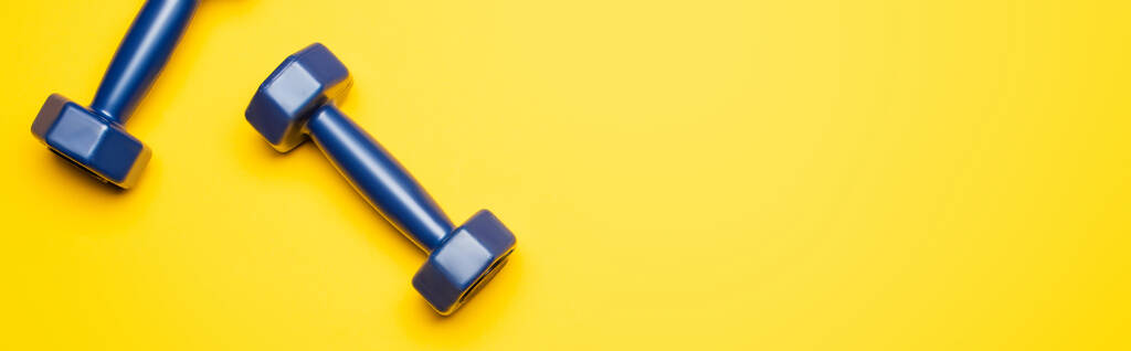 vista superior de halteres azuis no fundo amarelo, tiro panorâmico
 - Foto, Imagem