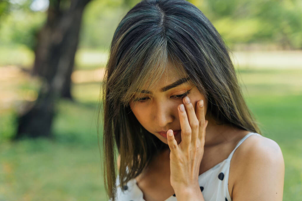 Nuori brunette nainen itkee ja pyyhkii kyyneleitä puistossa. Kaunis tyttö on onneton ja surullinen ulkona - Valokuva, kuva