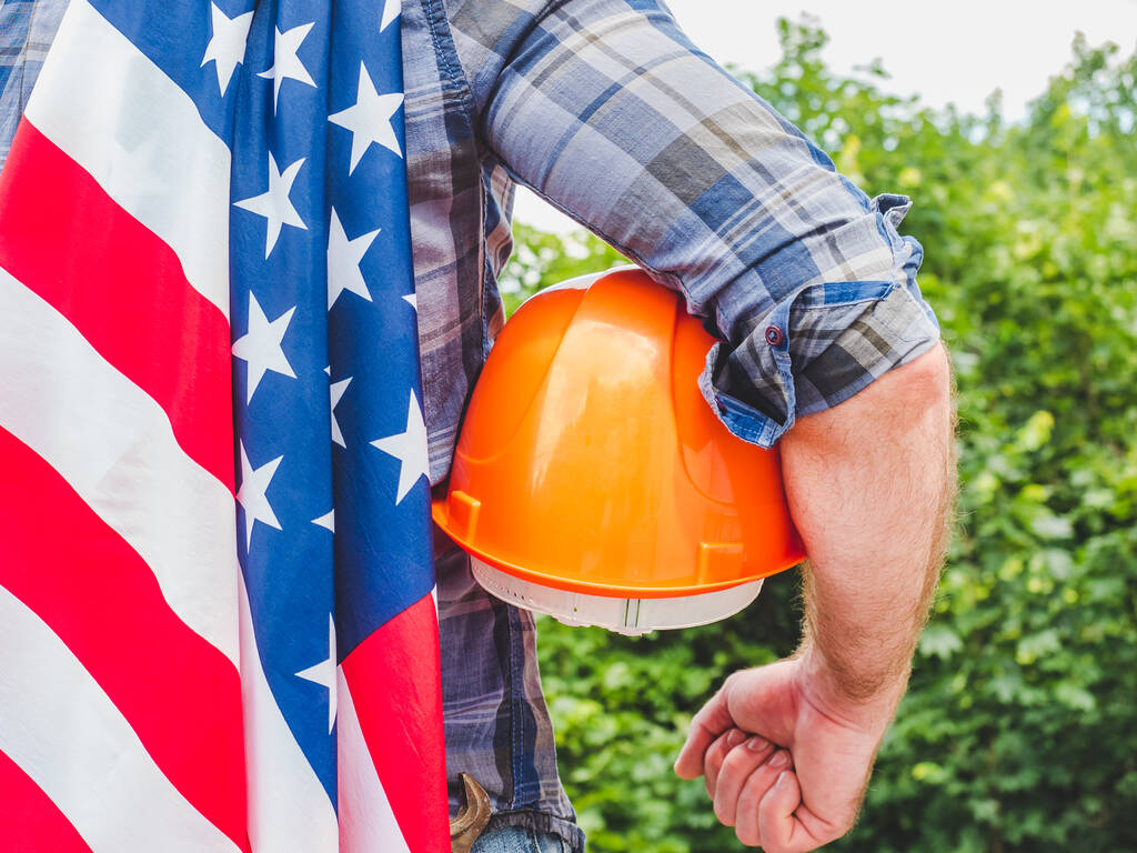 Homem bonito com ferramentas, segurando uma bandeira americana. Vista pelas traseiras, close-up. Conceito de trabalho e emprego
 - Foto, Imagem