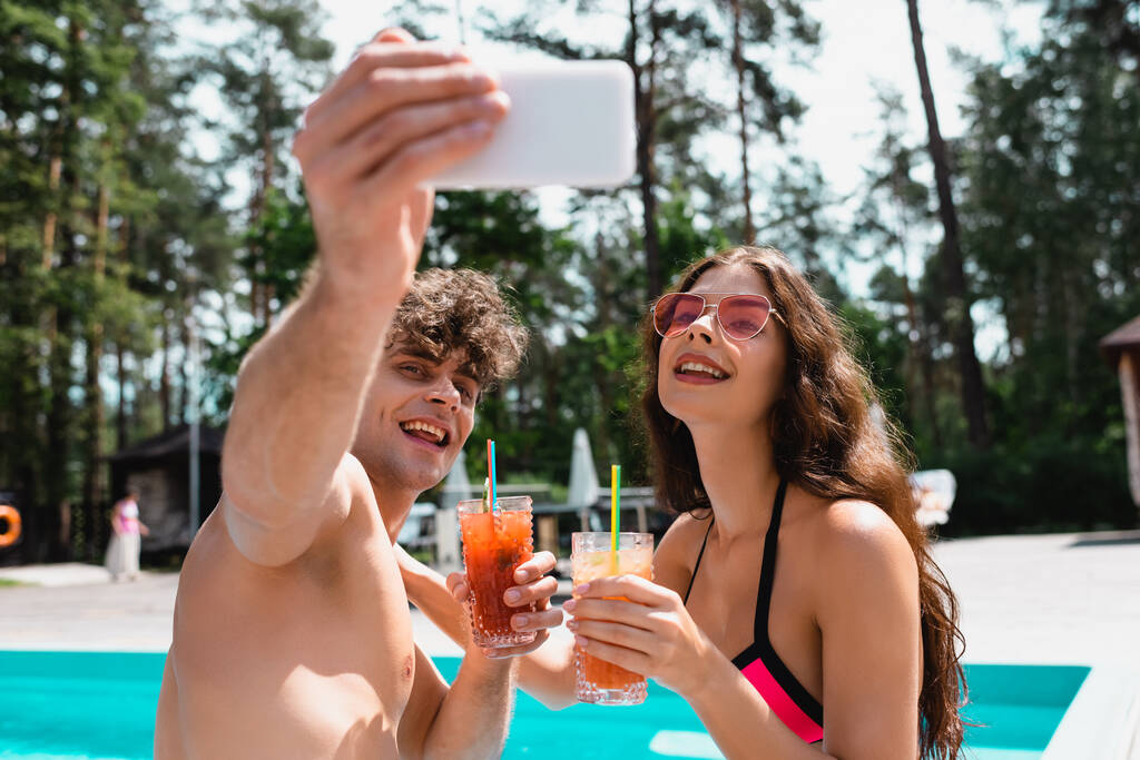 enfoque selectivo de hombre y mujer alegres en gafas de sol celebración de cócteles y tomar selfie
  - Foto, Imagen
