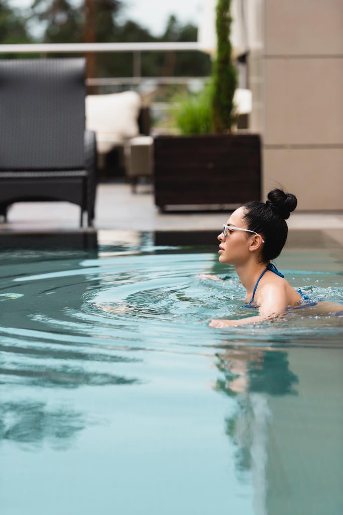 πλαϊνή άποψη του ελκυστική κοπέλα σε γυαλιά ηλίου κολύμπι στην πισίνα  - Φωτογραφία, εικόνα