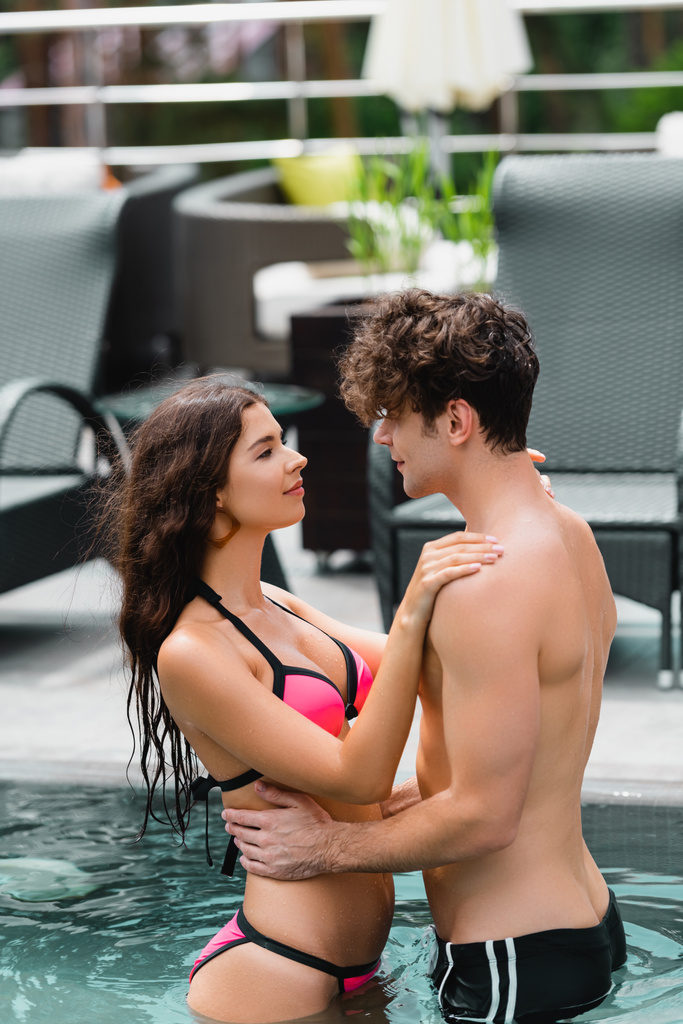 attraktive Frau umarmt gutaussehenden Mann ohne Hemd im Schwimmbad  - Foto, Bild