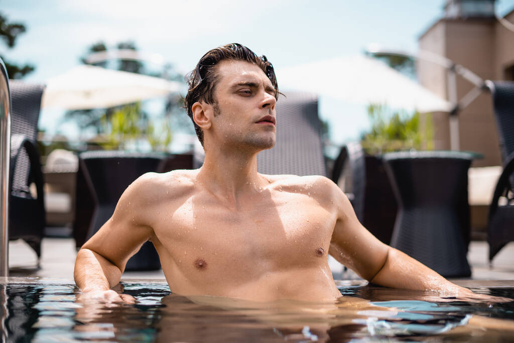 ημίγυμνος και σέξι άντρας που κοιτάζει αλλού στην πισίνα.  - Φωτογραφία, εικόνα