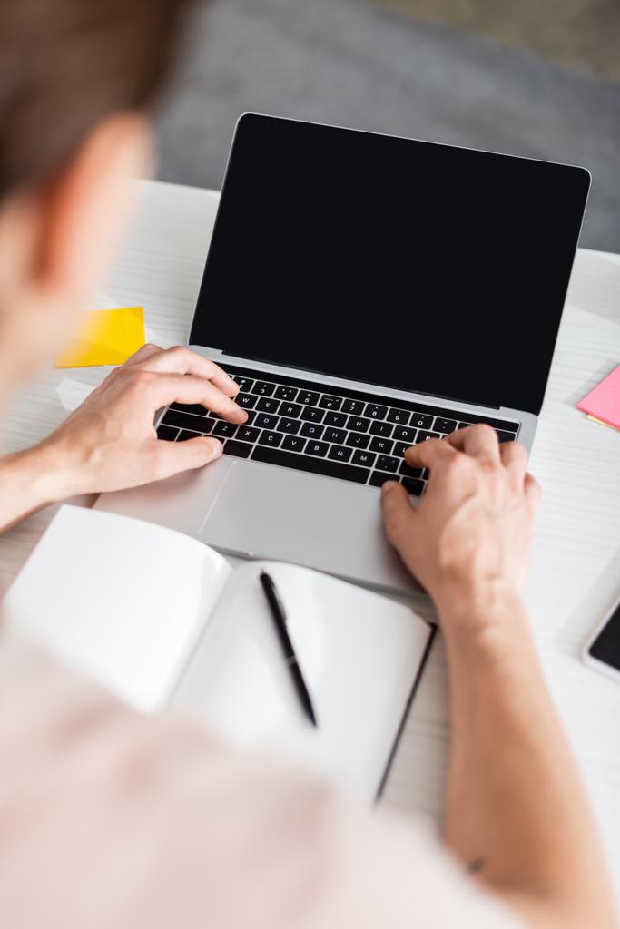 Обрезанный вид человека, печатающего на ноутбуке с пустым экраном, сидящего за столом дома, зарабатывая онлайн концепцию - Фото, изображение