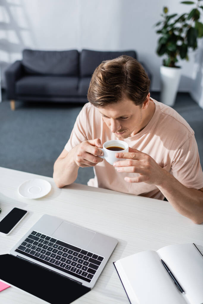 Overhead view of man drinking coffee and looking at laptop screen at home, earning online concept - Photo, Image