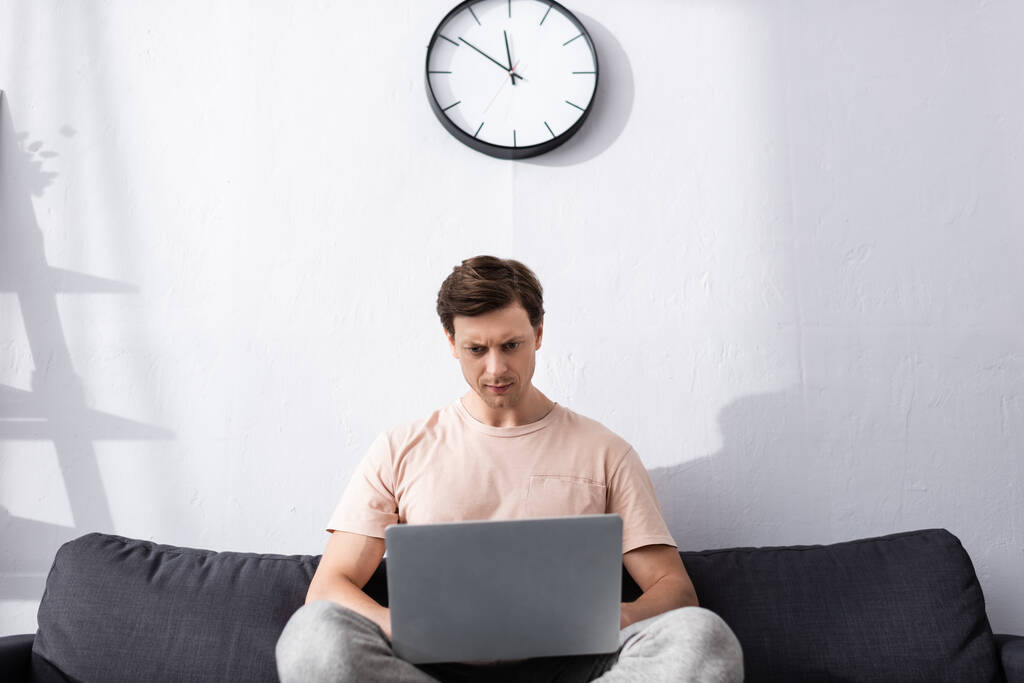 Επιλεκτική εστίαση του εστιασμένου ελεύθερου επαγγελματία χρησιμοποιώντας φορητό υπολογιστή, ενώ κάθεται στον καναπέ στο σπίτι, έννοια της απόκτησης online - Φωτογραφία, εικόνα