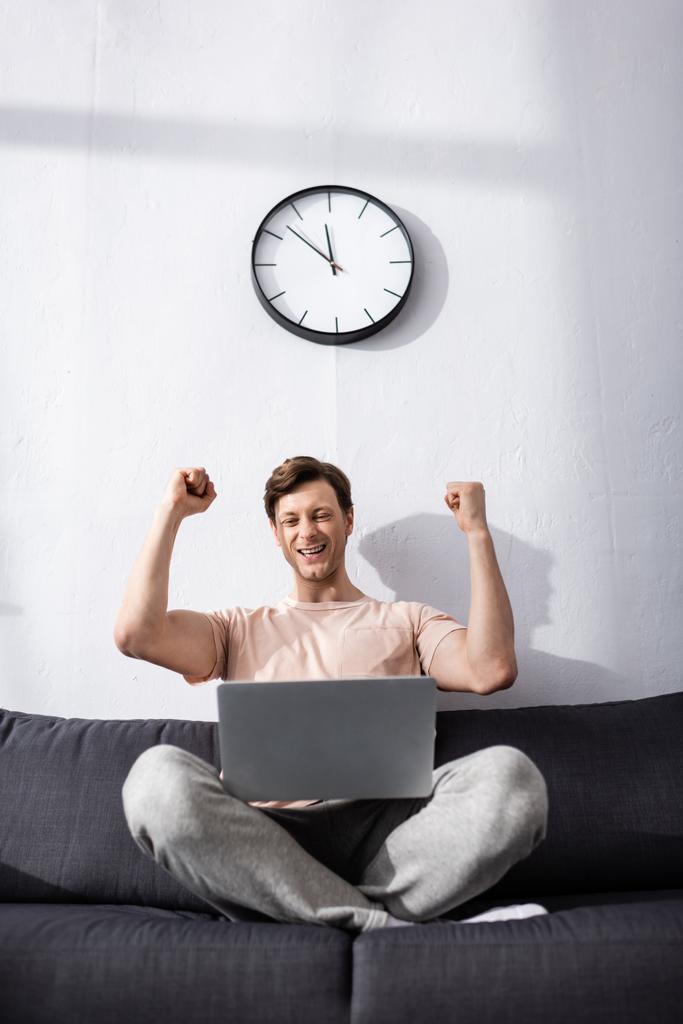 Cheerful freelancer showing yeah gesture and looking at laptop on sofa, earning online concept - Photo, Image