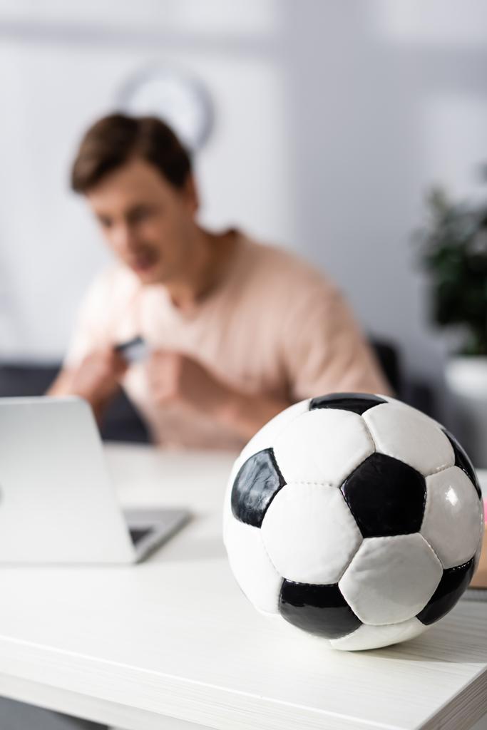 テーブルの上にサッカーの選択的な焦点と自宅でラップトップの近くに座っている男,オンラインで稼ぐの概念 - 写真・画像