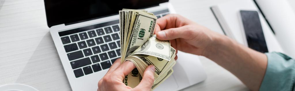 Panoramatické plodiny člověka počítání dolarů v blízkosti gadgets na stole, vydělávat online koncept - Fotografie, Obrázek