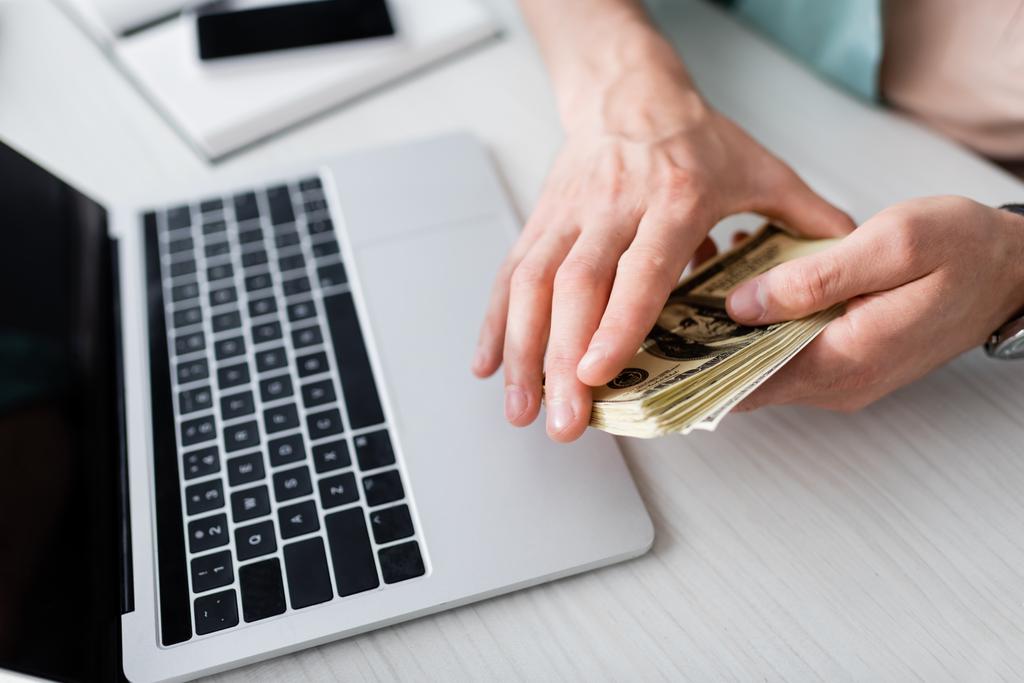 Cropped view of man holding cash near laptop on table, earning online concept - Photo, Image