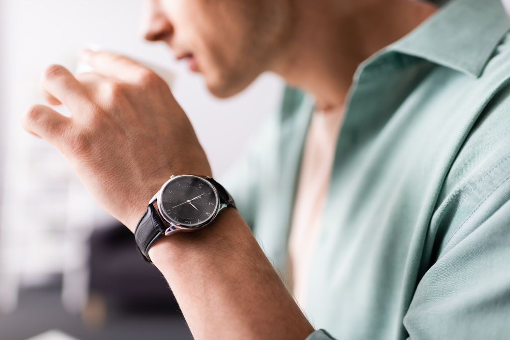 Vista ritagliata dell'uomo in orologio da polso bere caffè, concetto di gestione del tempo  - Foto, immagini