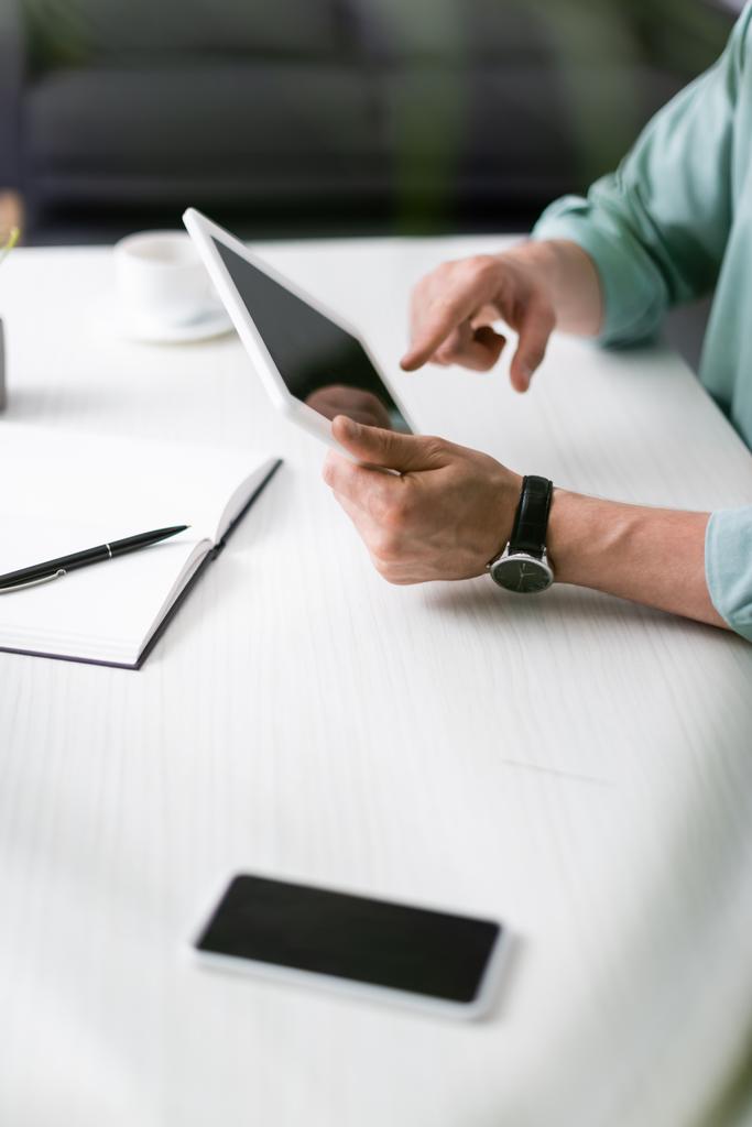 Gesneden weergave van de mens met behulp van digitale tablet naast smartphone en notebook op tafel, het verdienen van online concept - Foto, afbeelding