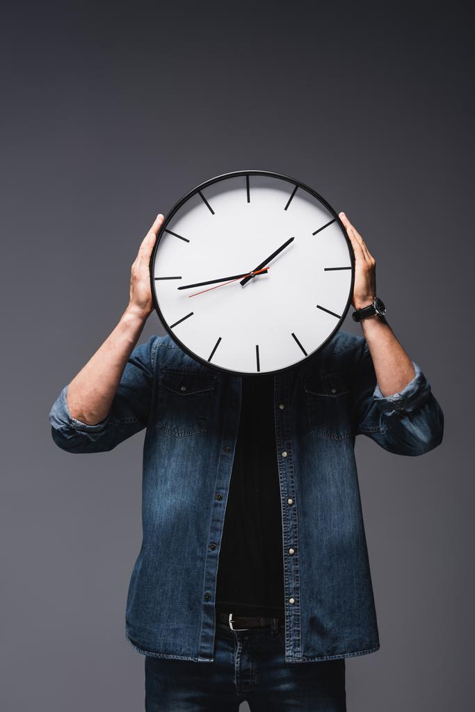 Молодий чоловік тримає годинник біля обличчя на сірому фоні, концепція управління часом
  - Фото, зображення