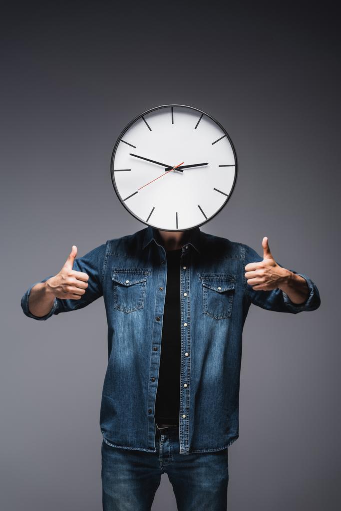 Muž s hodinami v blízkosti obličeje ukazující palce nahoru na šedém pozadí, koncept řízení času  - Fotografie, Obrázek