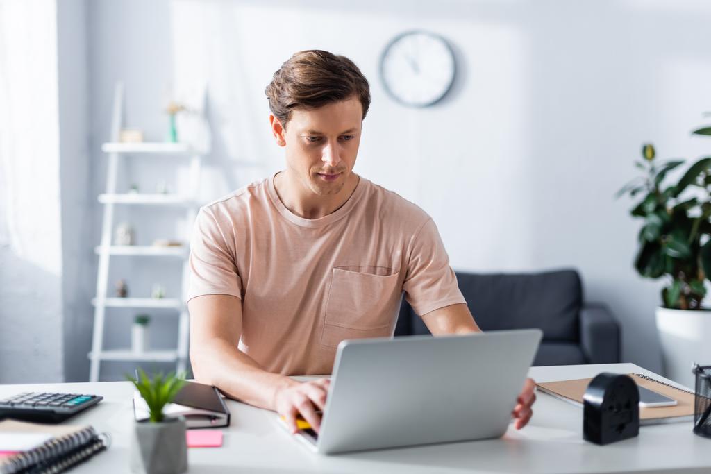 Selectieve focus van jonge man met behulp van laptop in de buurt briefpapier op tafel thuis, concept van het verdienen van online - Foto, afbeelding