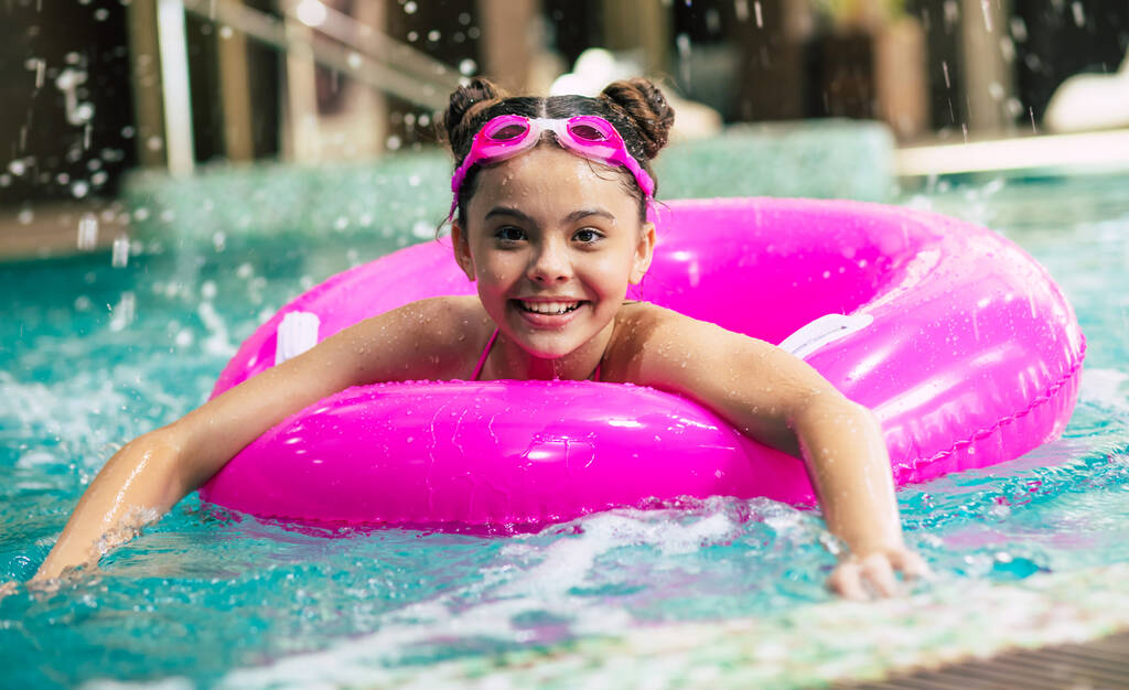 Gelukkig meisje met een bril spelend met een roze opblaasbare ring in het zwembad op een warme zomerdag. Kinderen leren zwemmen. Kinderwaterspeelgoed.Familie strandvakantie. - Foto, afbeelding