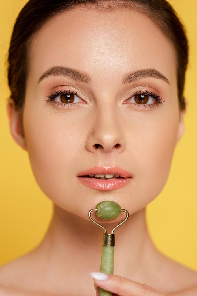 portrait of beautiful woman using jade roller on face isolated on yellow - Photo, Image