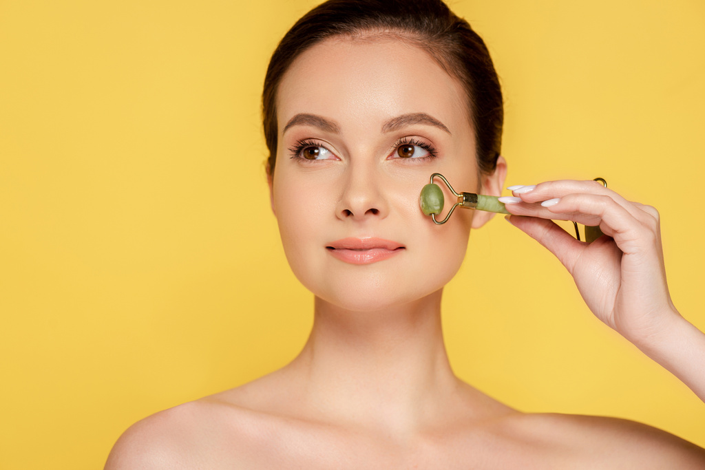 beautiful naked woman using jade roller on face isolated on yellow - Photo, Image