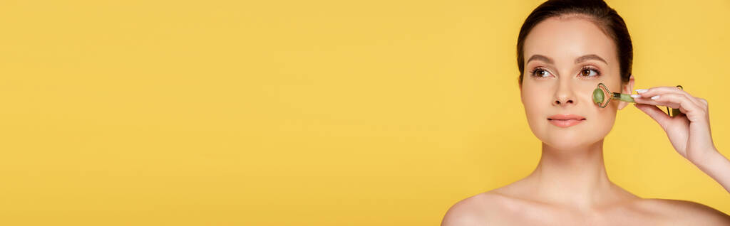 beautiful naked woman using jade roller on face isolated on yellow, panoramic shot - Photo, Image