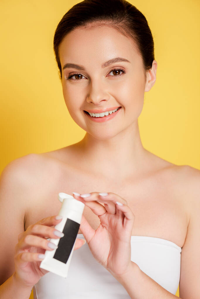beautiful brunette smiling woman holding hand cream isolated on yellow - Photo, Image