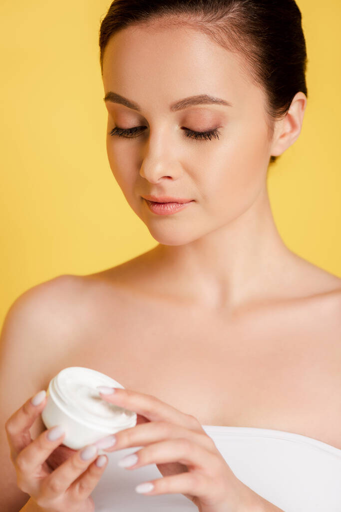 beautiful woman holding container with cosmetic cream isolated on yellow - Photo, Image