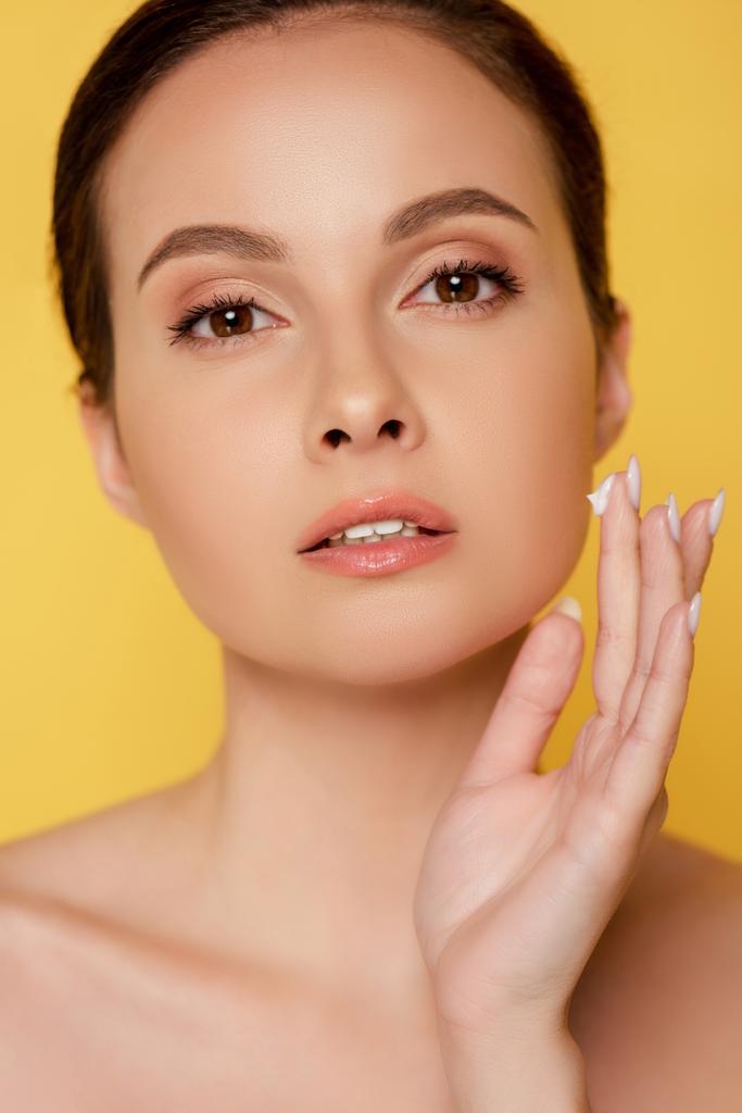 nackte schöne Frau Anwendung Gesichtscreme isoliert auf gelb - Foto, Bild