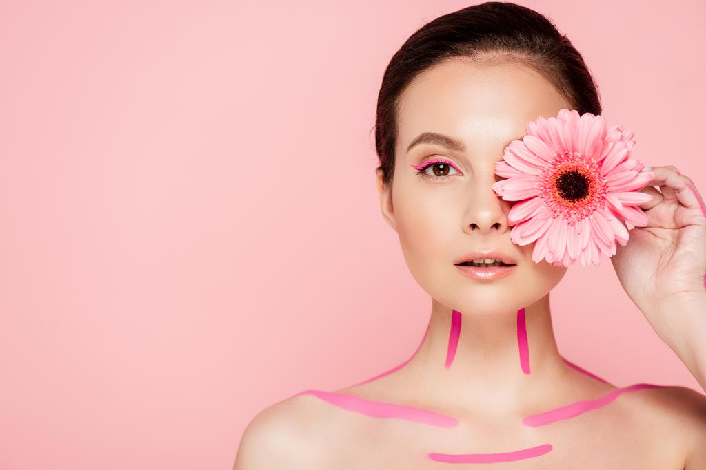 γυμνή όμορφη γυναίκα με ροζ γραμμές στο σώμα και χρυσάνθεμο κοντά στο μάτι απομονώνονται σε ροζ - Φωτογραφία, εικόνα