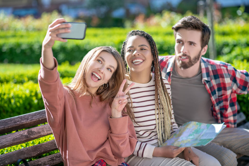 Ragazza con smartphone scattare selfie con gli amici in panchina. - Foto, immagini