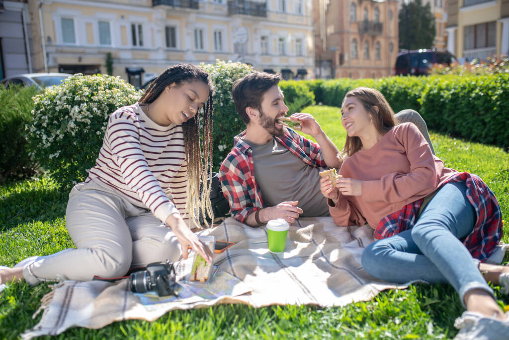 Dos chicas y un tipo comiendo sándwiches en un picnic
 - Foto, Imagen